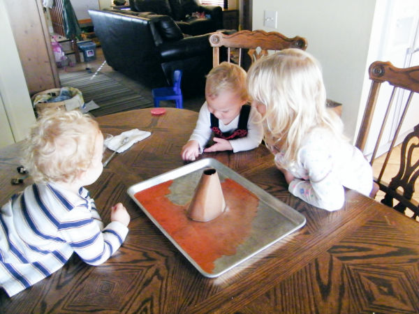 Three kids observing the volcano experiment after it erupted from the baking soda and vinegar.