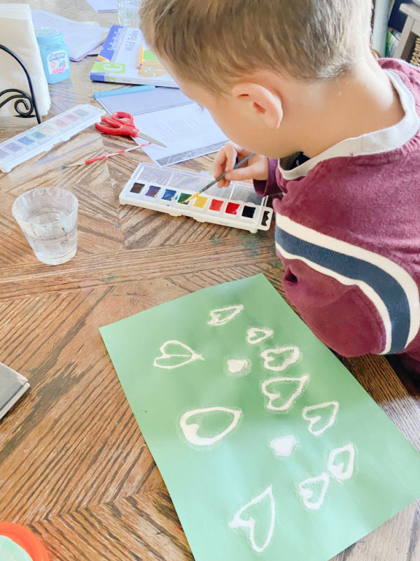 Salt and glue hearts on green construction paper. Child dipping paintbrush into watercolor paints.