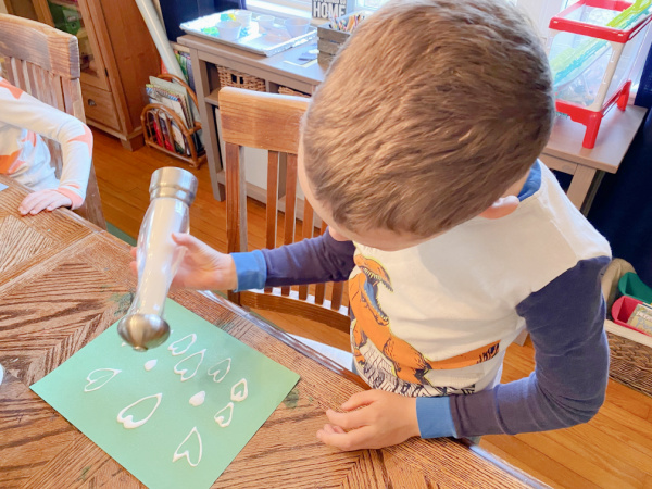 Child sprinkling salt onto glue hearts he drew on a piece of construction paper. 