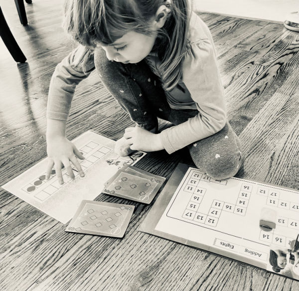 Girl playing math games on the floor. In homeschooling and life, if it feels like too much, it probably is.