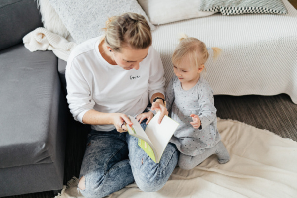 Mom reading to 18-month-old toddler. Article is list of stay-at-home mom activities for 18-month-old toddlers.