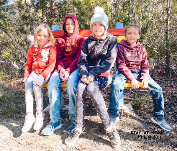 Four kids sitting on a bench in a natural setting. 