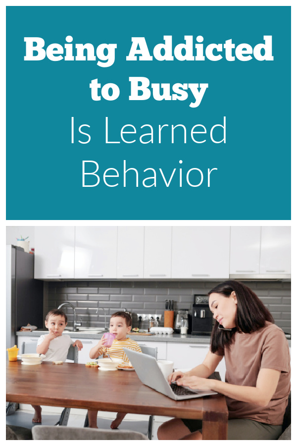 Mom working at the kitchen table with two children nearby. Text reads being addicted to busy is learned behavior.