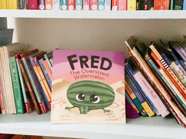 Picture of a book called Fred the Oversized Watermelon on a children's bookshelf. Article contains ideas for teaching children that they are loved.