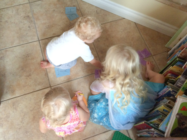 Kids on the floor arranging letter cards in order for teaching toddlers to spell their name.