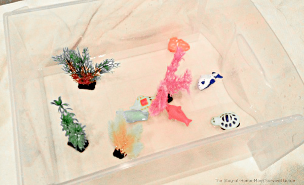 Five dollar sensory bin idea as an activity for kids when it is too hot to play outdoors. Bin contains aquarium plants and plastic dollar store fish toys.