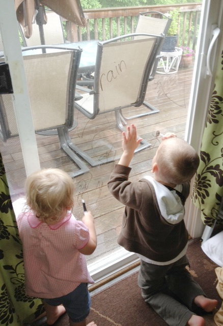 Children drawing on the windows with dry erase markers is an indoor activity for the days when it is too hot or rainy to play outside.