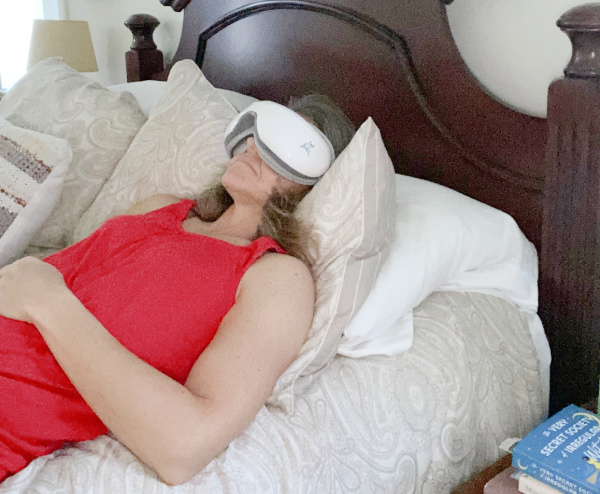 Lying down in bed with the Bob and Brad EyeOasis 2 eye massager on to relax.