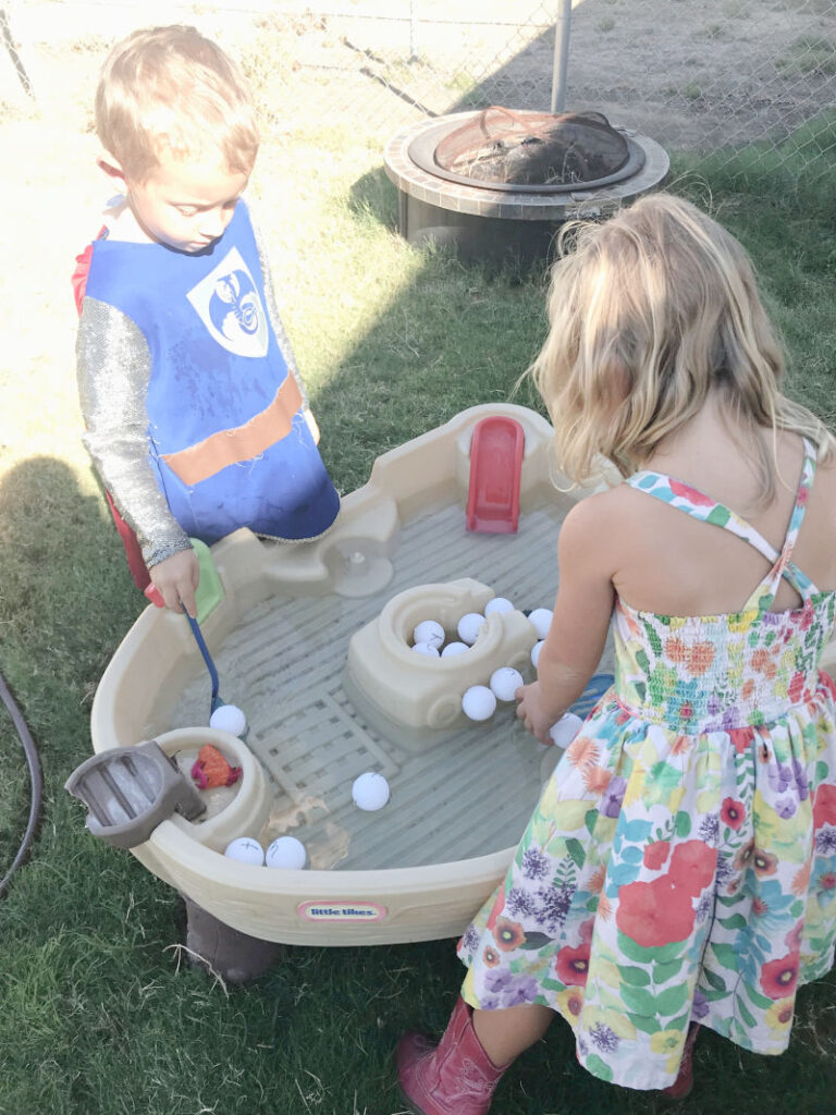 Two preschoolers scooping ping pong balls from a water table. Ping pong ball letter match learning activity for preschool.